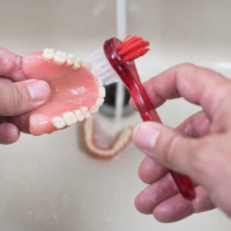 a person is scrubbing their affordable dentures with a special brush to clean them