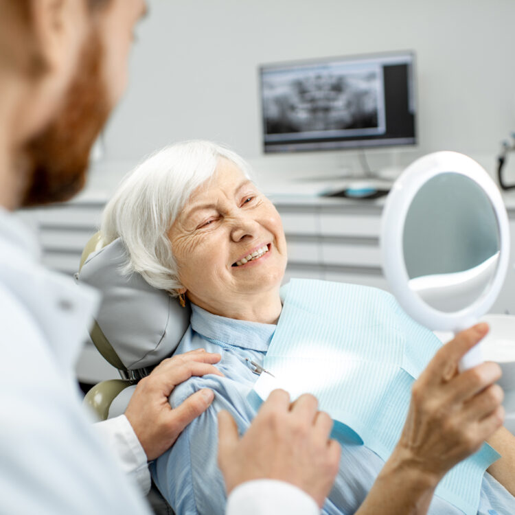 a woman smiling in a mirror after her affordable dentures were delivered