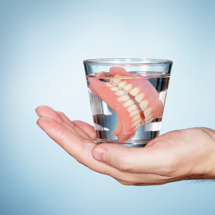 a set of affordable dentures in a cup of water for maintenance